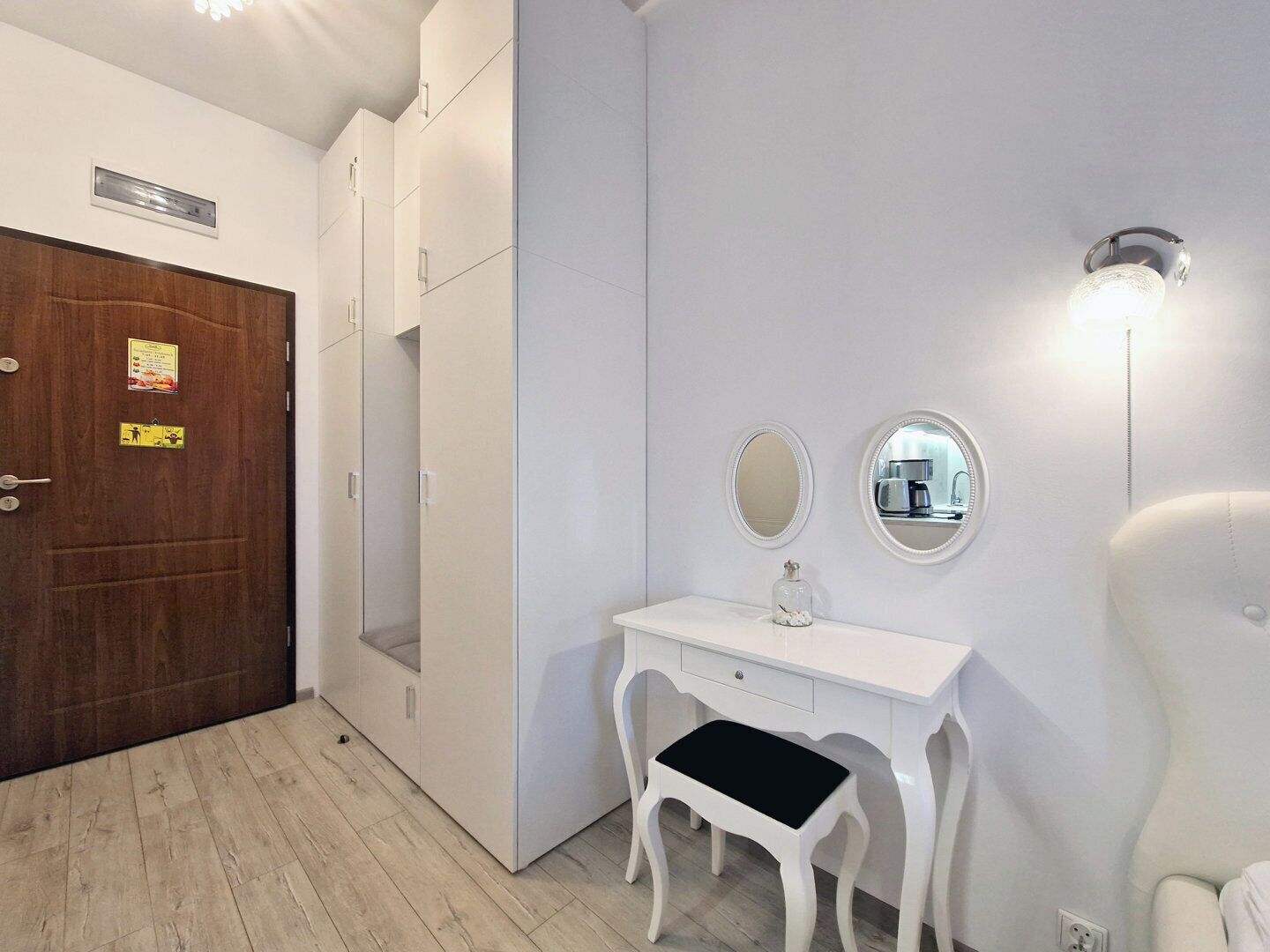 Un baño moderno con un tocador blanco, dos espejos, un taburete pequeño y un accesorio de luz fijado a la pared.