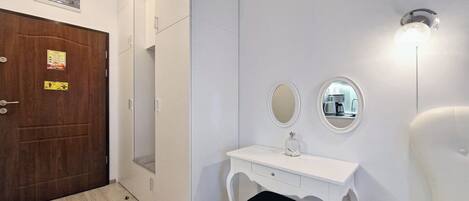 A modern bathroom with a white vanity, two mirrors, a small stool, and a wall-mounted light fixture.