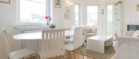 Una sala de estar moderna con comedor, muebles blancos, ventanas amplias y un balcón.