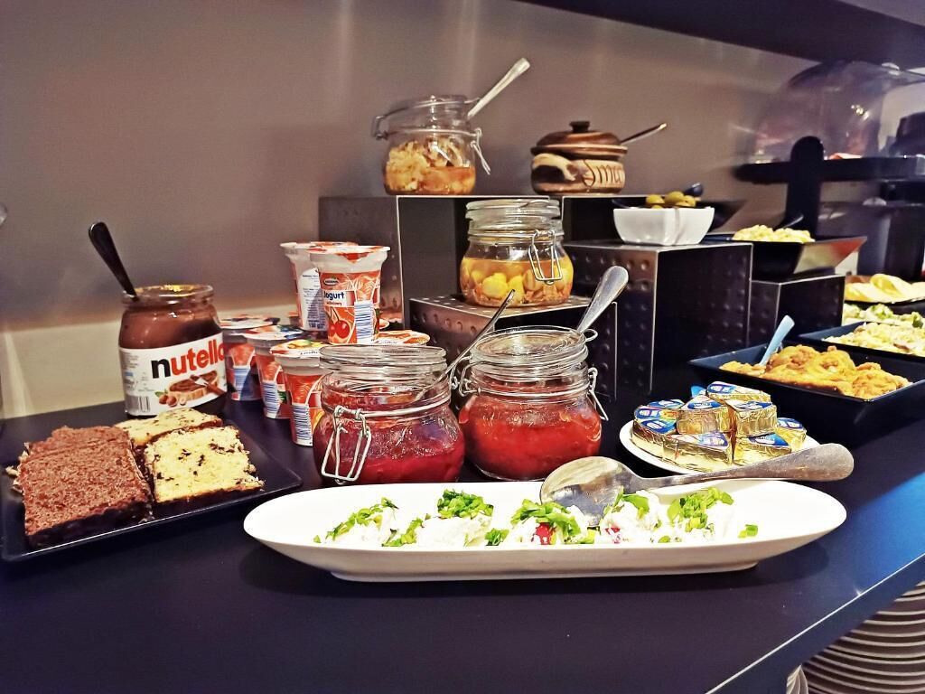 Un bufé con diferentes opciones de comida, incluyendo frascos con salsas, una ensalada en un plato y bandejas de postres.