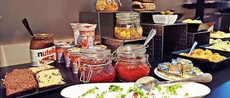 Un bufé con diferentes opciones de comida, incluyendo frascos con salsas, una ensalada en un plato y bandejas de postres.