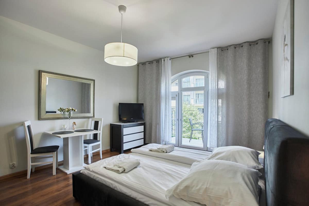Une chambre à coucher comprenant un lit, un bureau, une chaise, un téléviseur et une fenêtre avec des rideaux.