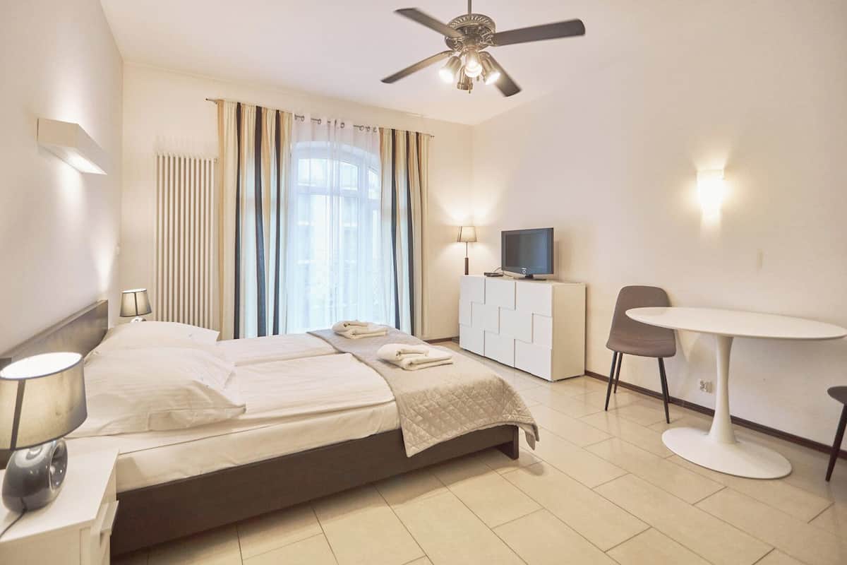 Une chambre d’hôtel équipée d’un lit, d’un bureau, d’une chaise, d’une télévision et d’un ventilateur de plafond.