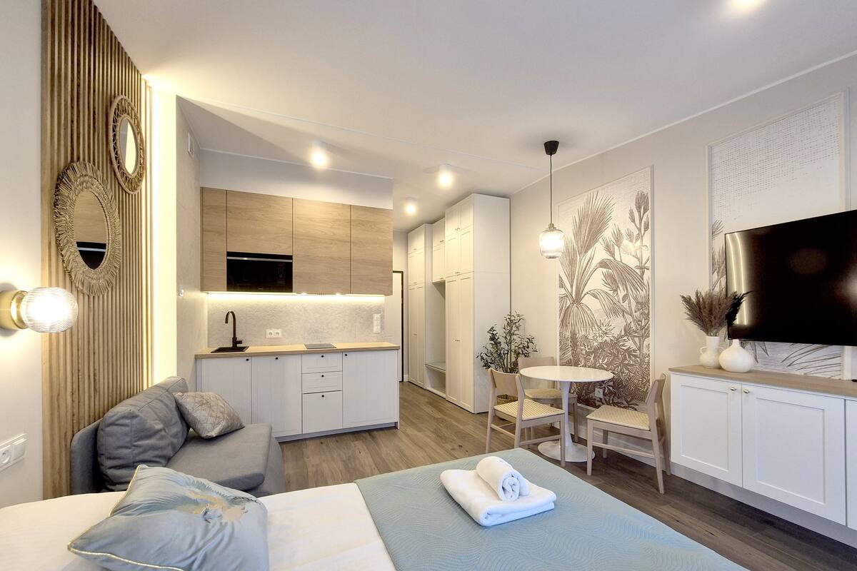 Une chambre d’hôtel moderne comprenant un lit, un coin salon avec une table et des chaises, une kitchenette et un téléviseur fixé au mur.