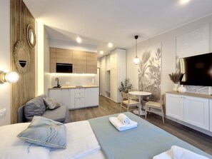 A modern hotel room with a bed, a seating area with a table and chairs, a kitchenette, and a TV mounted on the wall. - Regina Maris by Baltic Home (Swinoujscie)