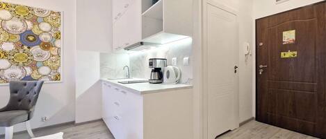 A compact kitchen with a built-in stove, a coffee maker, and a sink. There is a door with a sign on it, and a wall-mounted light fixture.
