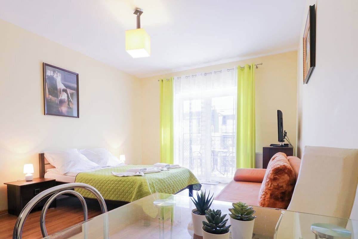 Une chambre d’hôtel moderne, dotée d’un lit, d’une table en verre, de plantes en pot et offrant une vue sur la ville grâce à de grandes fenêtres.
