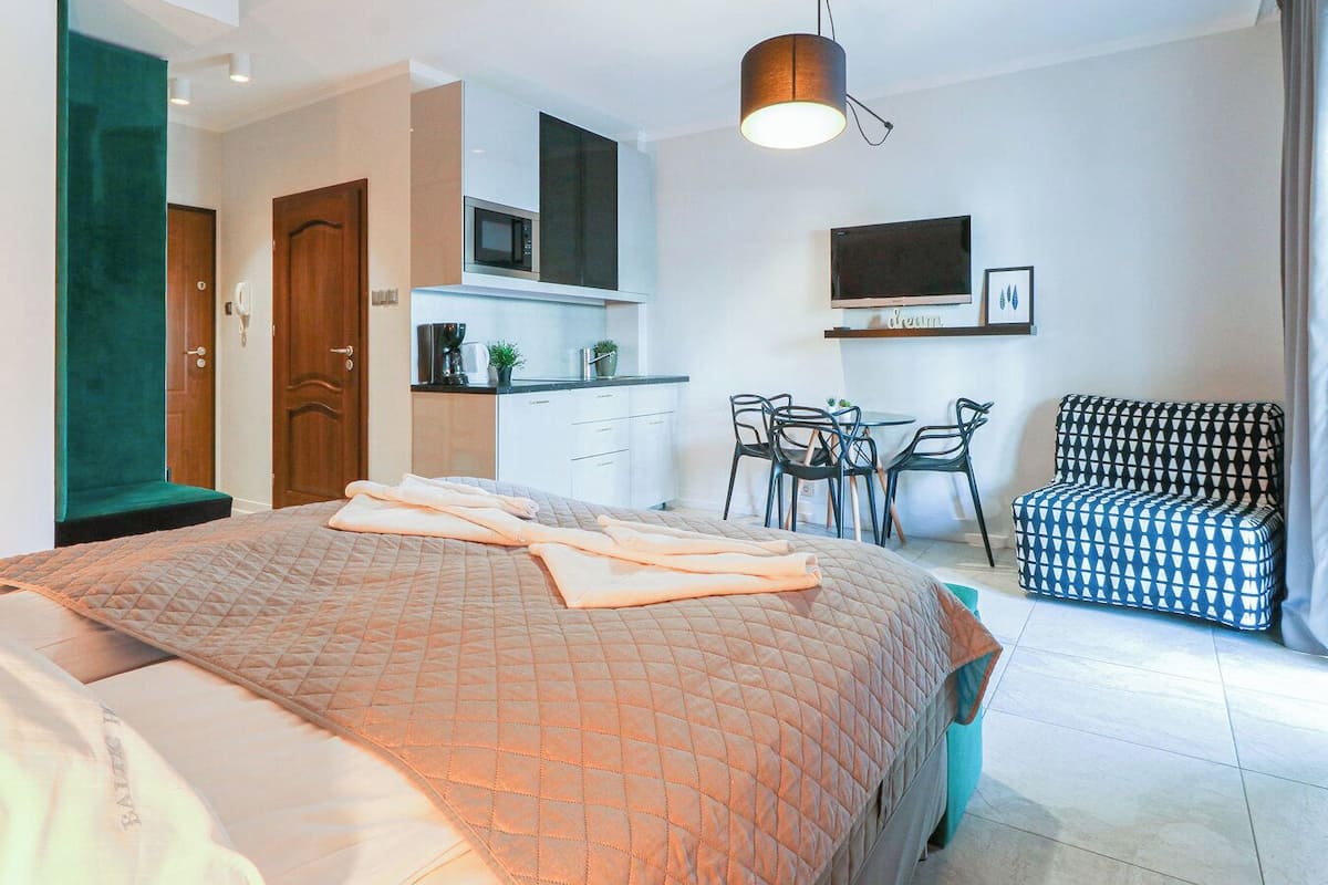 Une chambre avec un lit, un coin cuisine, un espace repas avec des chaises et un téléviseur fixé au mur.