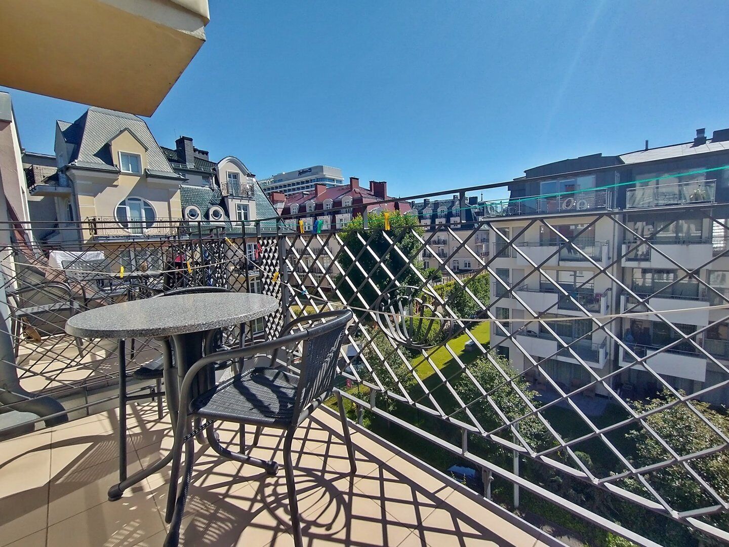 A balcony with a round table and chairs, a metal fence, and buildings in the background.
