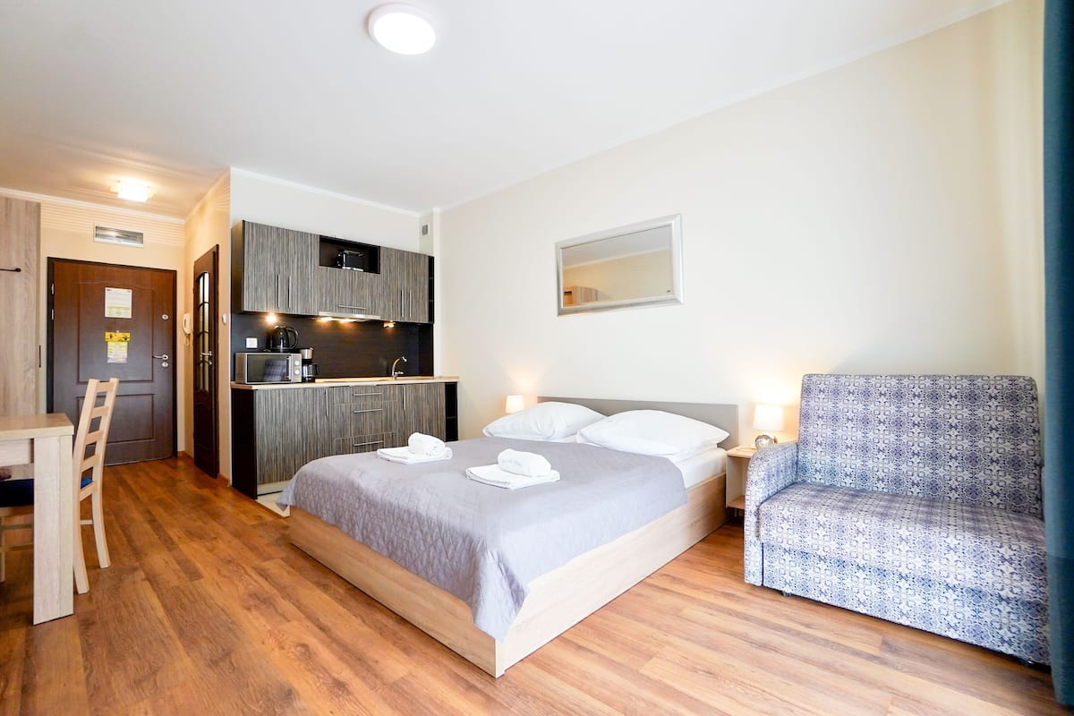 Une chambre d’hôtel de taille réduite, comprenant un lit, une chaise, un petit bureau et une kitchenette.