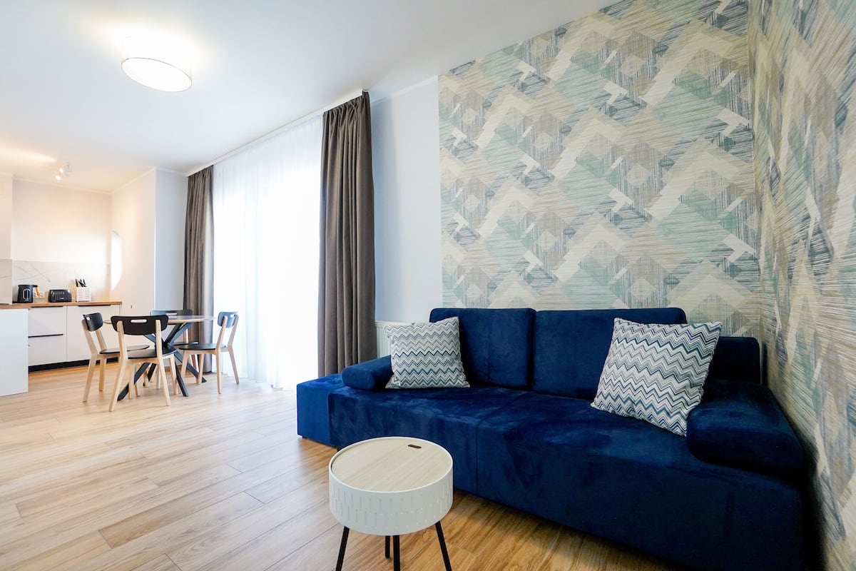Un salon moderne avec un canapé bleu, un pouf rond blanc et un coin repas comprenant une table et des chaises.
