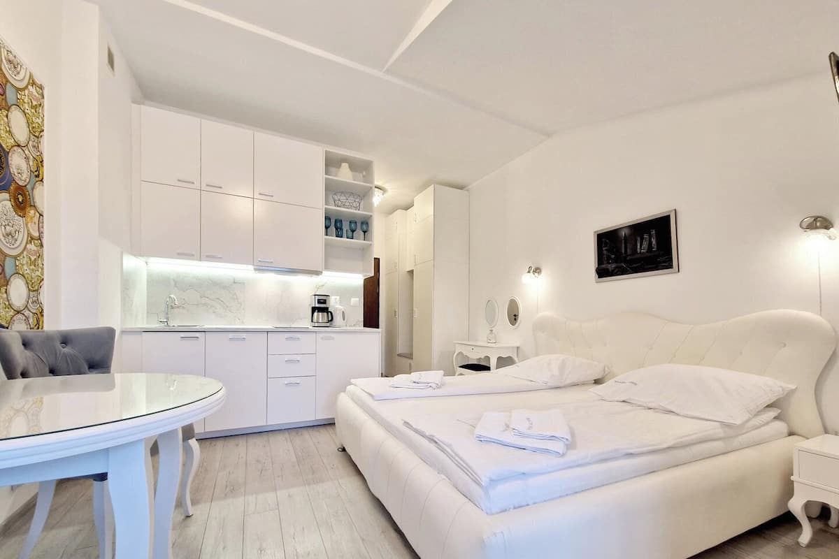 Une chambre moderne avec un grand lit, des tables de chevet, un petit bureau et un coin cuisine équipé de placards et d’une machine à café.
