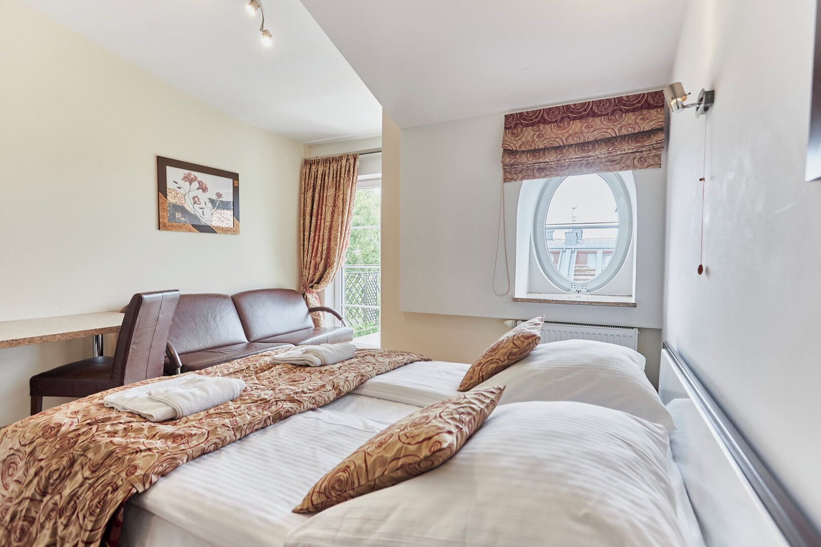 A hotel room with a bed, a sofa, a window with a view, and a painting on the wall.