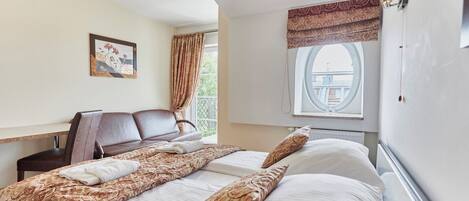 A hotel room with a bed, a sofa, a window with a view, and a painting on the wall.