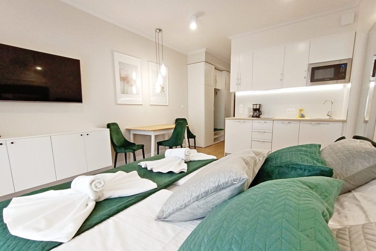 Une chambre d’hôtel équipée d’un lit, d’un bureau, d’une chaise, d’une kitchenette et d’un téléviseur fixé au mur.