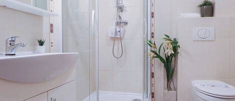 Un baño moderno con ducha de vidrio, un lavamanos blanco y un inodoro.