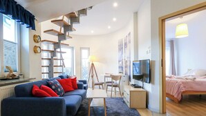 A modern living room with a blue sofa, wooden staircase, and a TV. - Regina Maris by Baltic Home (Swinoujscie)