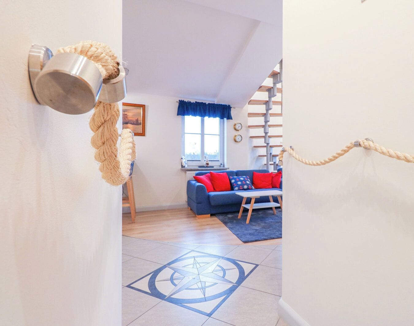 A cozy living room with a blue sofa, a wooden staircase, and a nautical-themed decor including a rope wall hanging.
