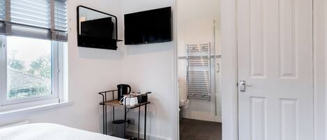 A bedroom with a bed, a TV mounted on the wall, a window with blinds, and a door leading to a bathroom.