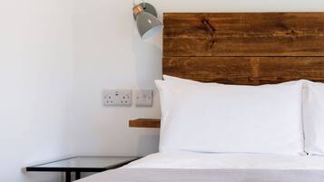 Un dormitorio con cabecera de madera, ropa de cama blanca, una mesita de noche y una lámpara de pared.