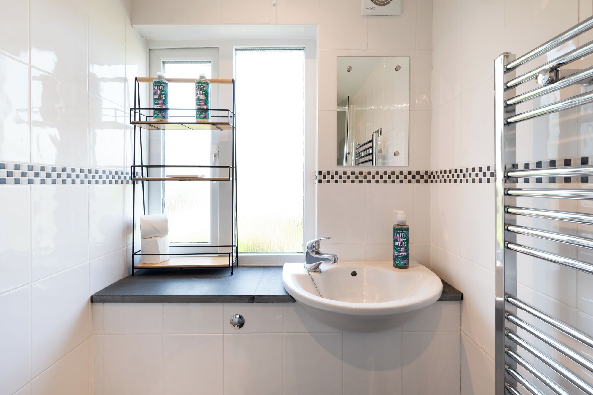 A bathroom with a white sink, a mirror, and a shelf with toiletries.