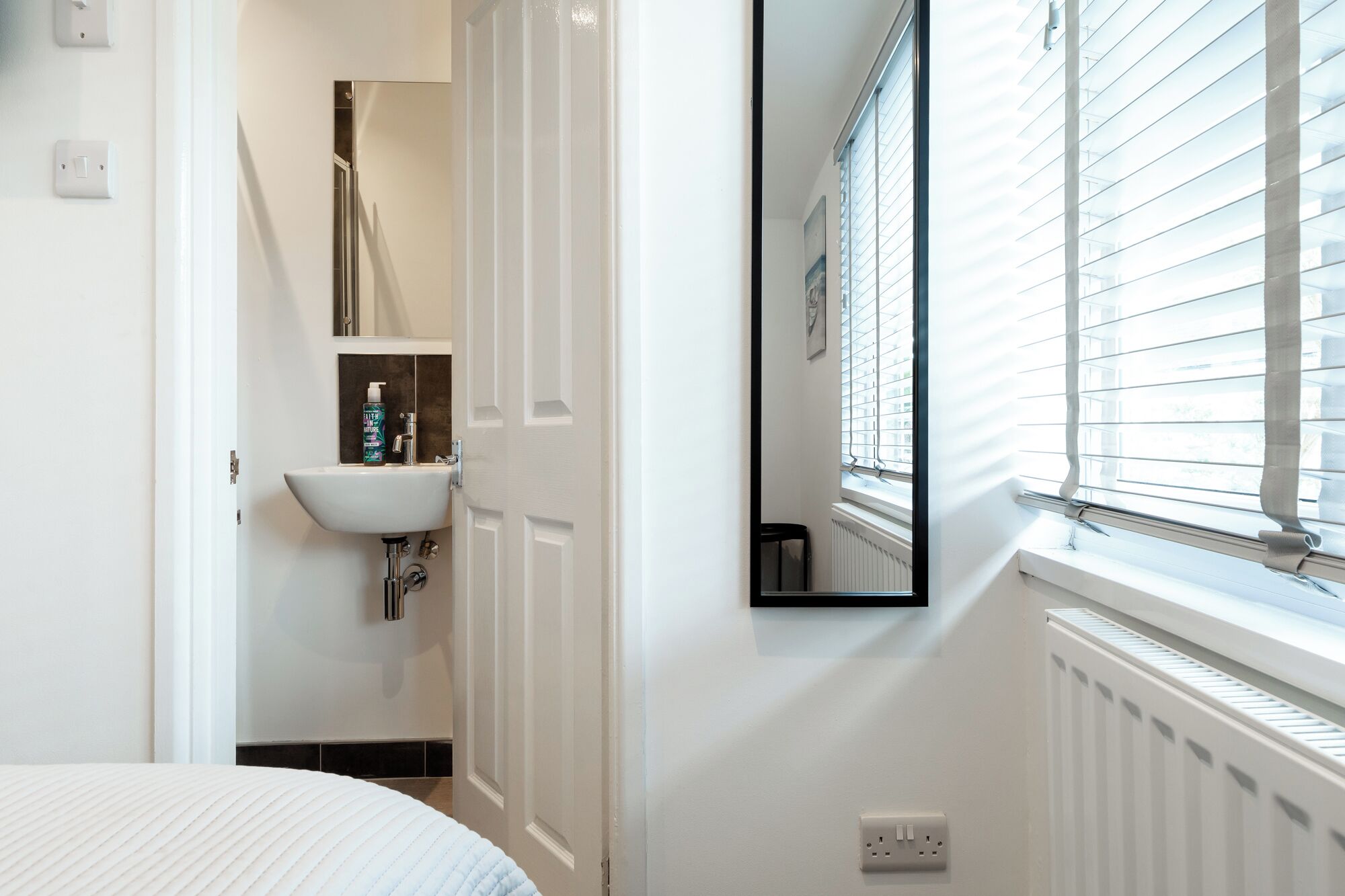 A modern bathroom with a white sink, a mirror, and a window with blinds.