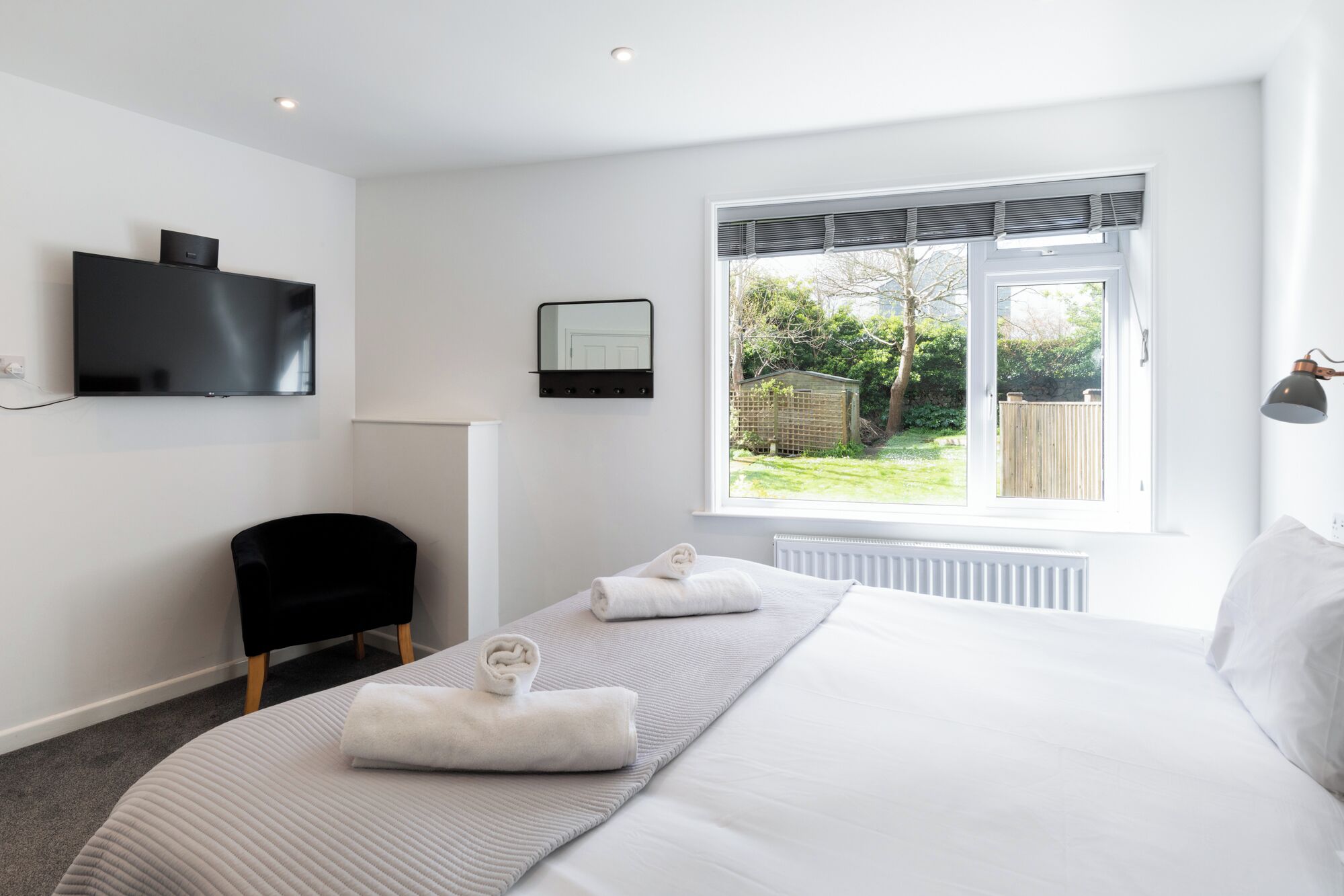 Une chambre moderne avec un grand lit, un téléviseur à écran plat, un fauteuil et une fenêtre donnant sur le jardin.