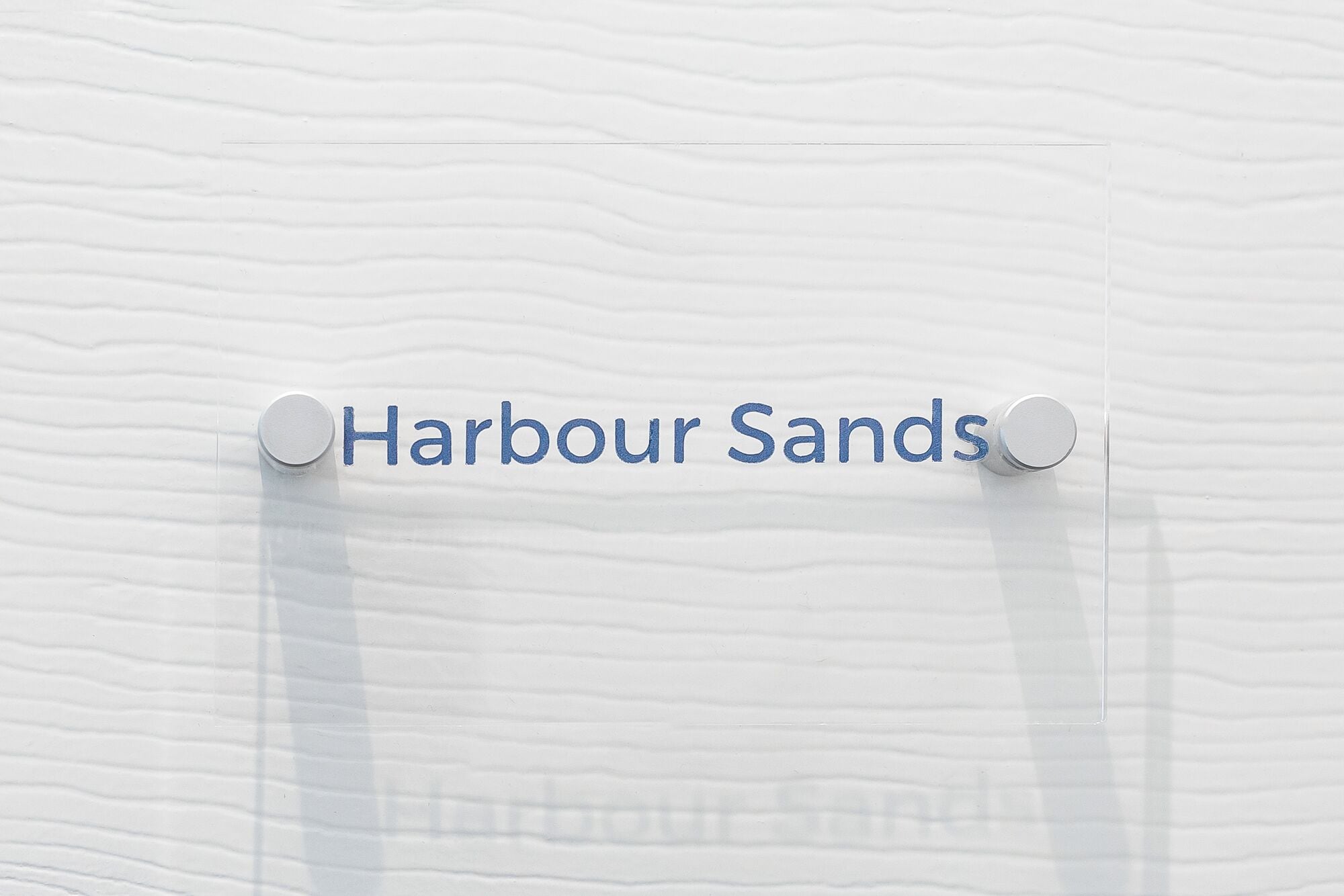 Une enseigne portant l’inscription « Harbour Sands » est fixée à un mur à texture.