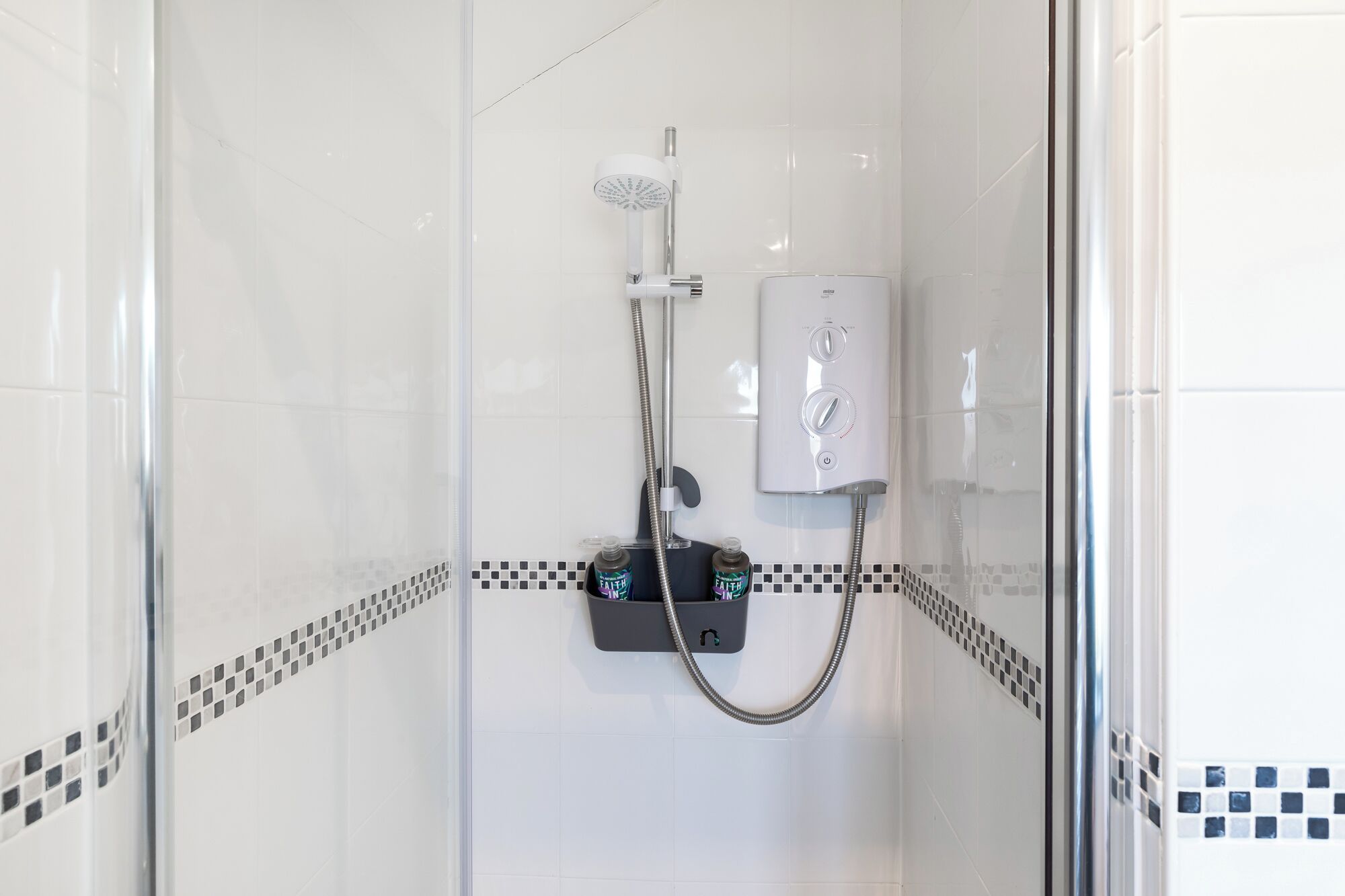 A glass-enclosed shower with a handheld showerhead and a wall-mounted control panel.