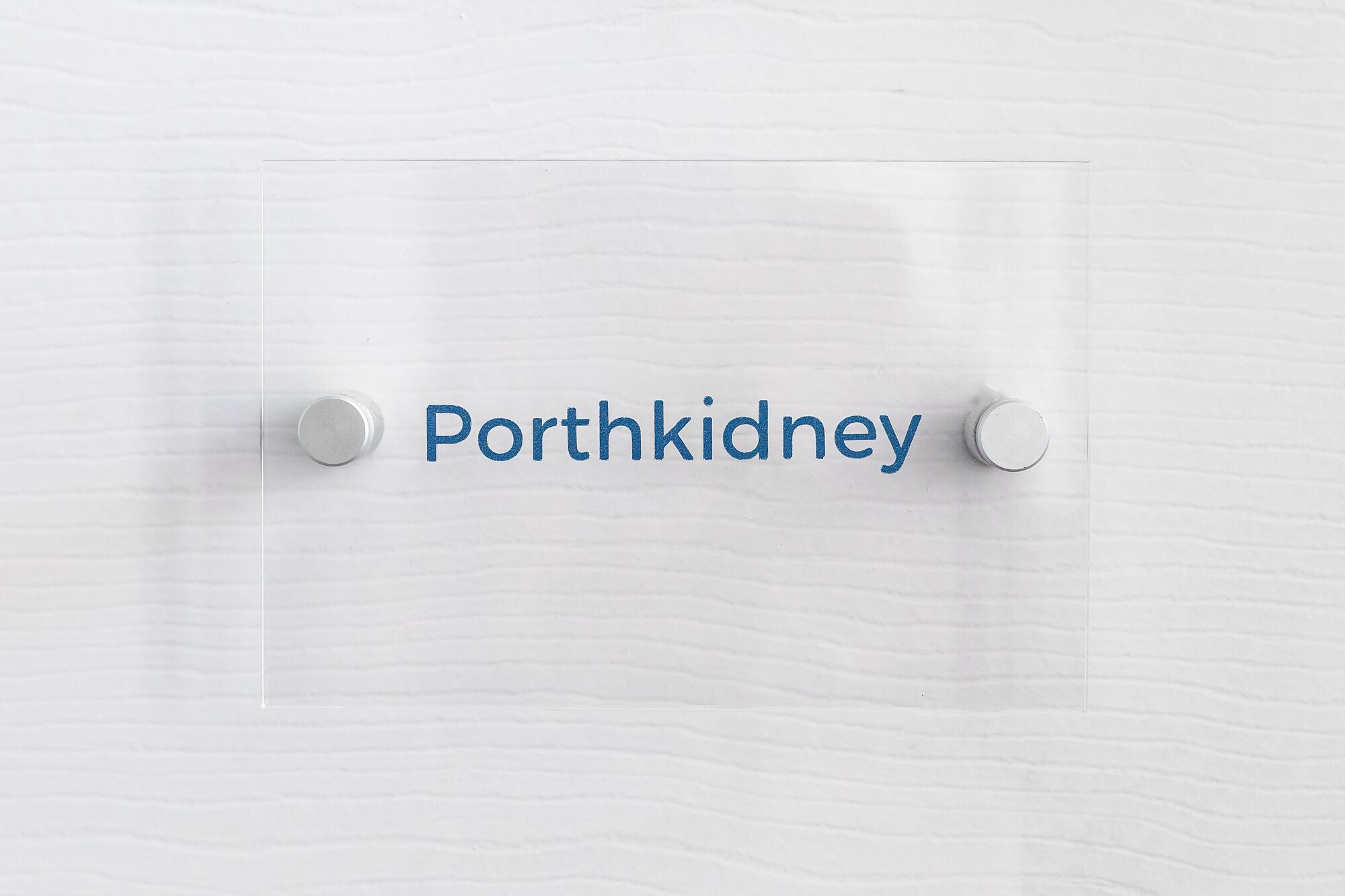 Une surface en bois peinte en blanc, portant l’inscription « Porthkidney » et ornée de deux poignées rondes en métal.