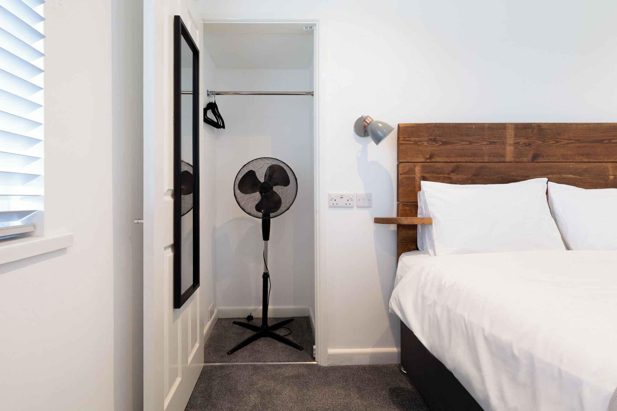 Ein Schlafzimmer mit einem Bett, einem Standventilator, einem Kleiderständer und einer Tür zu einem Badezimmer.
