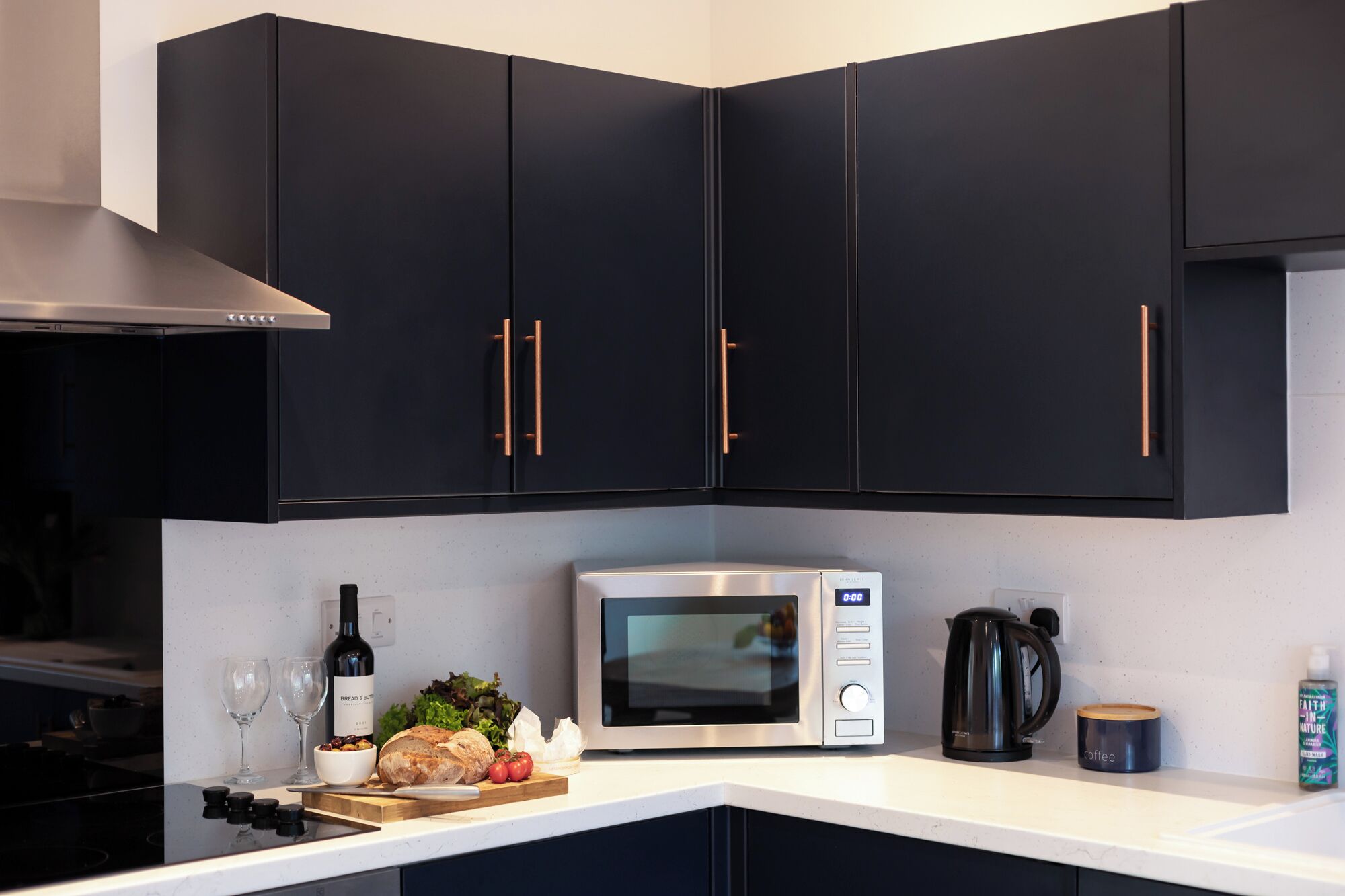 A kitchen with dark cabinets, a microwave, a kettle, and a coffee maker.
