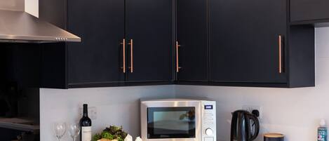 A kitchen with dark cabinets, a microwave, a kettle, and a coffee maker.