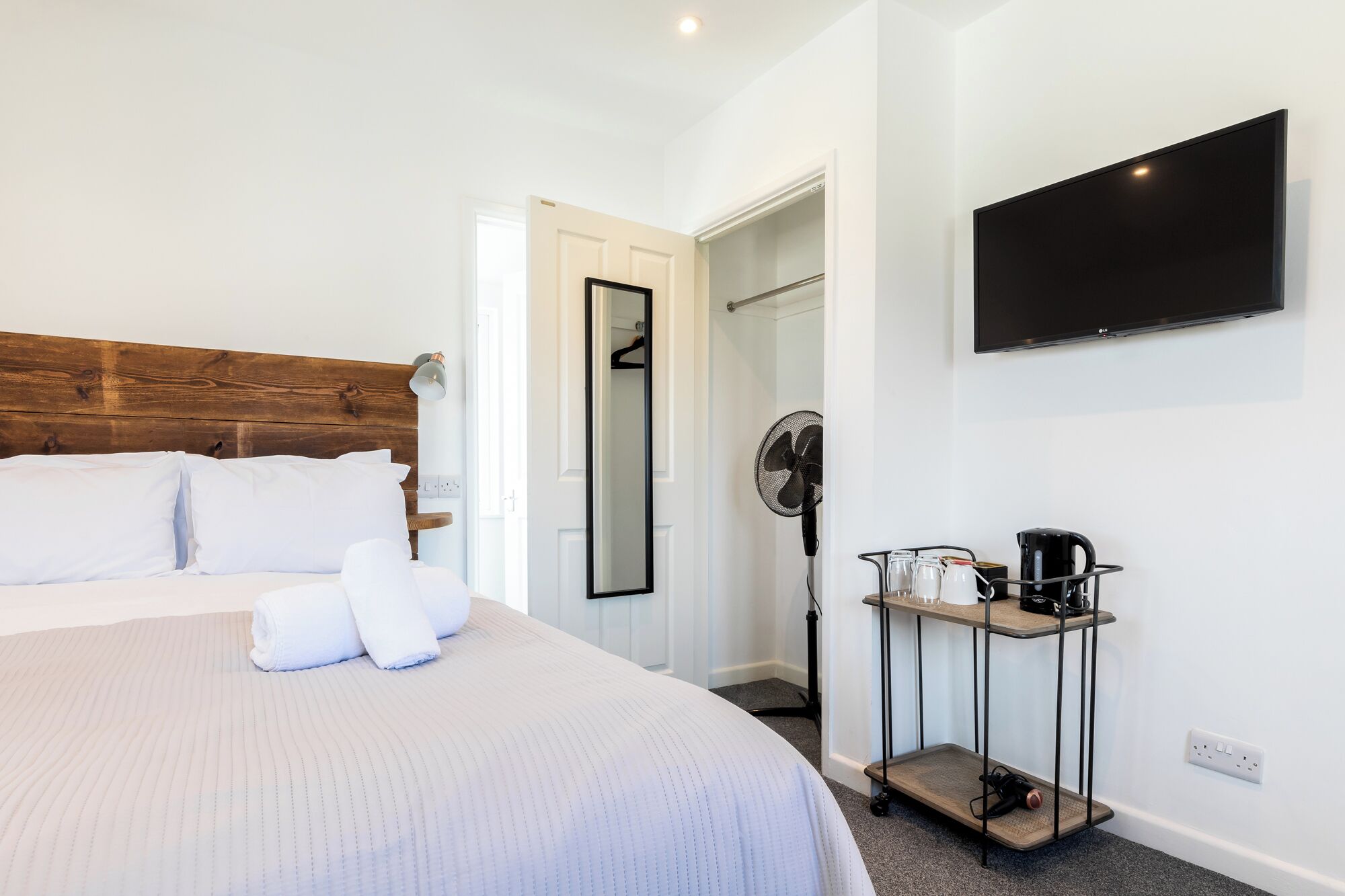 A hotel room with a large bed, a TV mounted on the wall, a fan, and a coffee station.