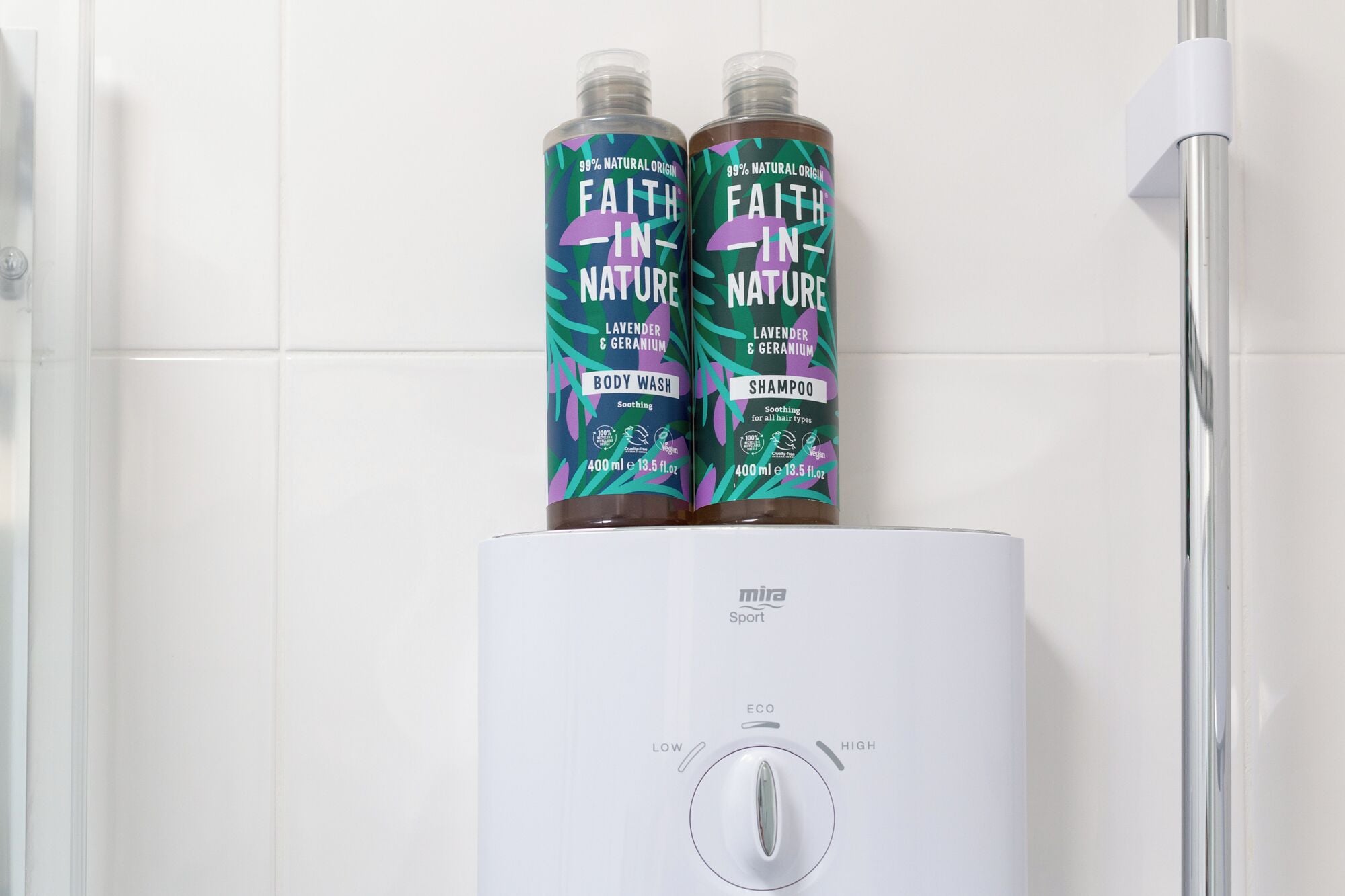 Ducha con dos botellas de jabón corporal y champú Faith-in-Nature encima.