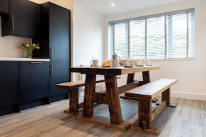 Una cocina moderna con armarios oscuros, una mesa de madera y una ventana con persianas.
