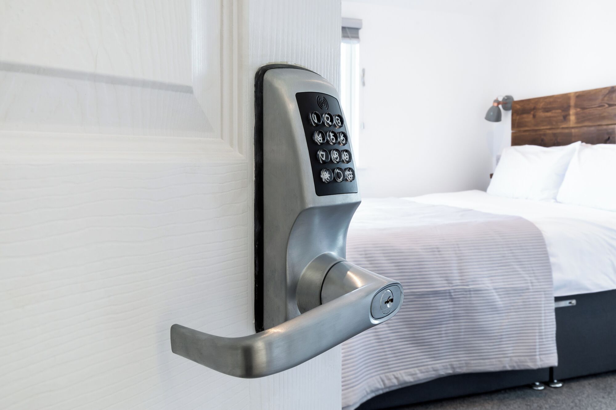 Une chambre d’hôtel moderne, équipée d’un lit, d’une tête de lit en bois et d’une serrure électronique fixée au mur.