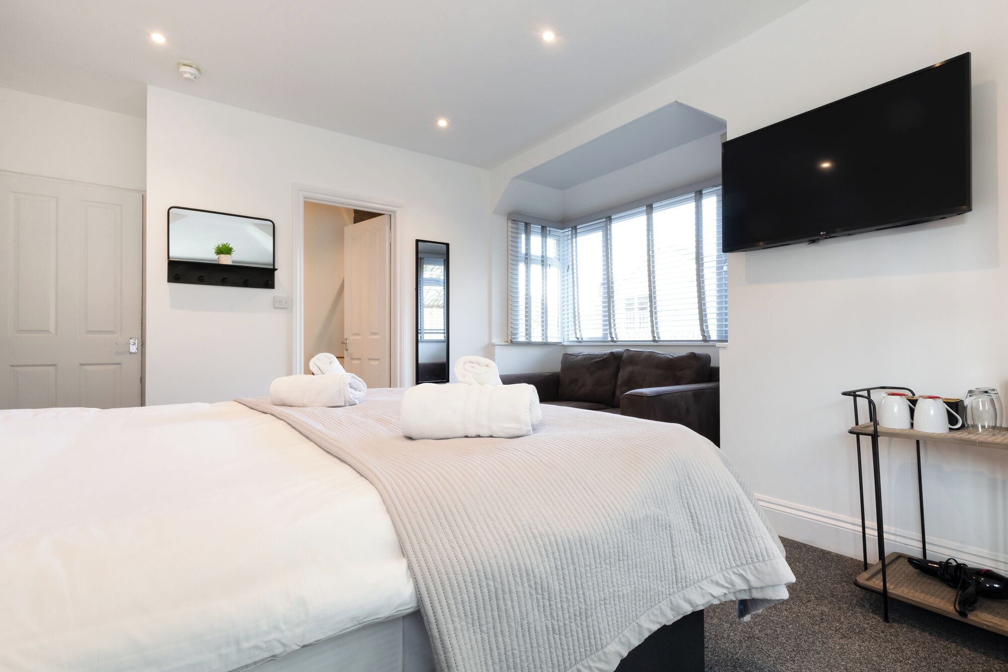Une chambre d’hôtel moderne dotée d’un grand lit, d’un téléviseur à écran plat fixé au mur et d’une fenêtre avec des stores.