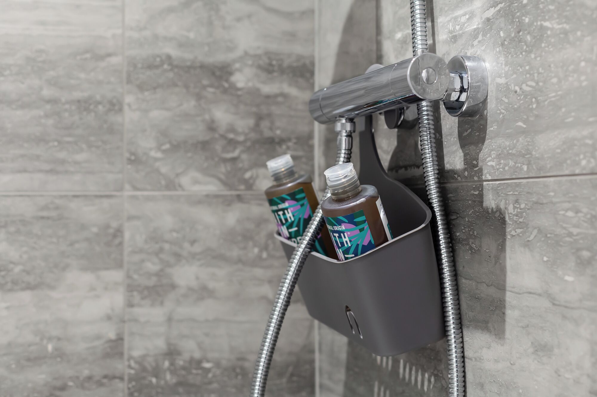 Una ducha con cabezal de ducha de mano y dos botellas de champú en un dispensador.