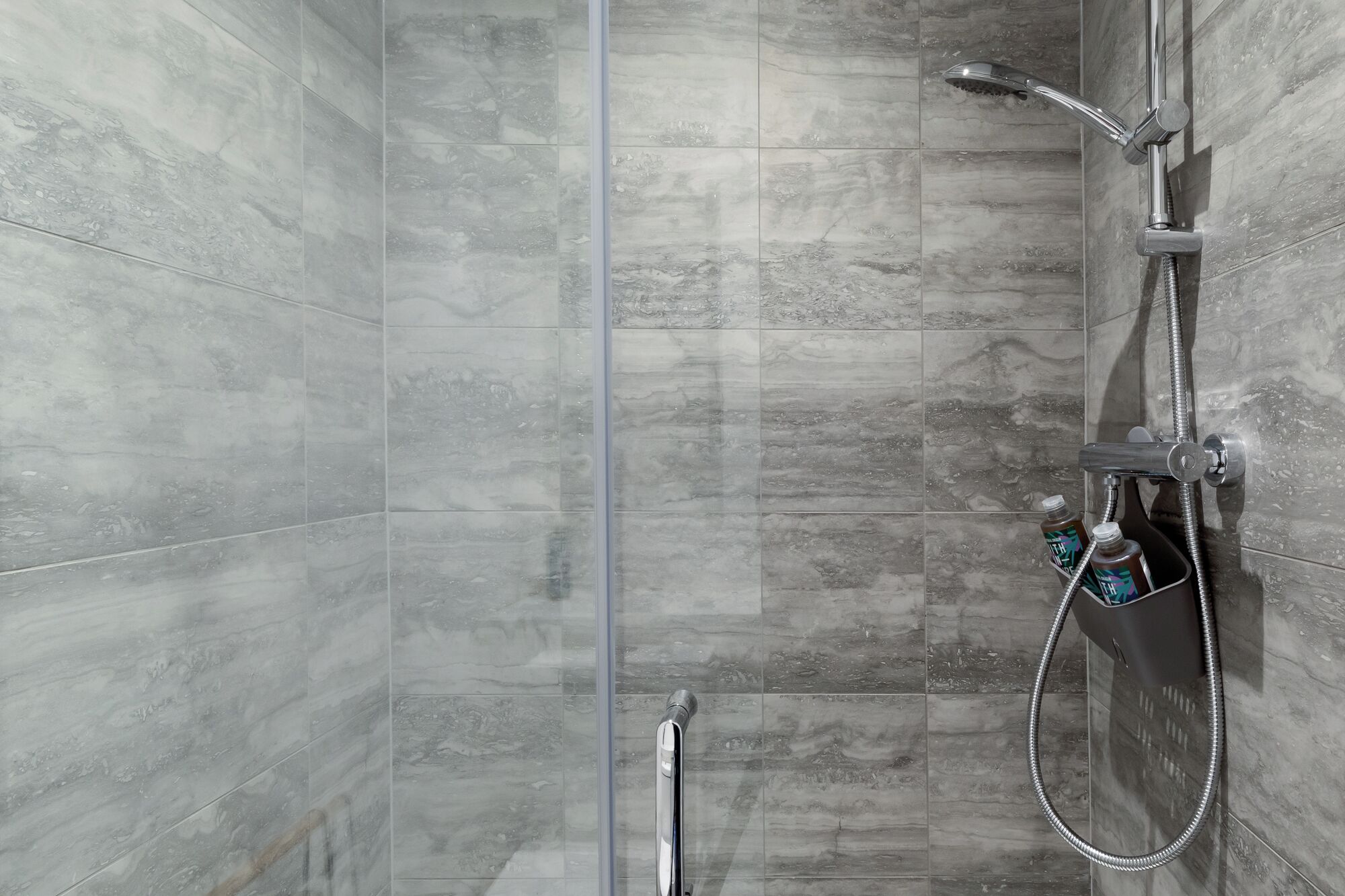 A shower area with grey marble tiles, a handheld showerhead, and a wall-mounted faucet.
