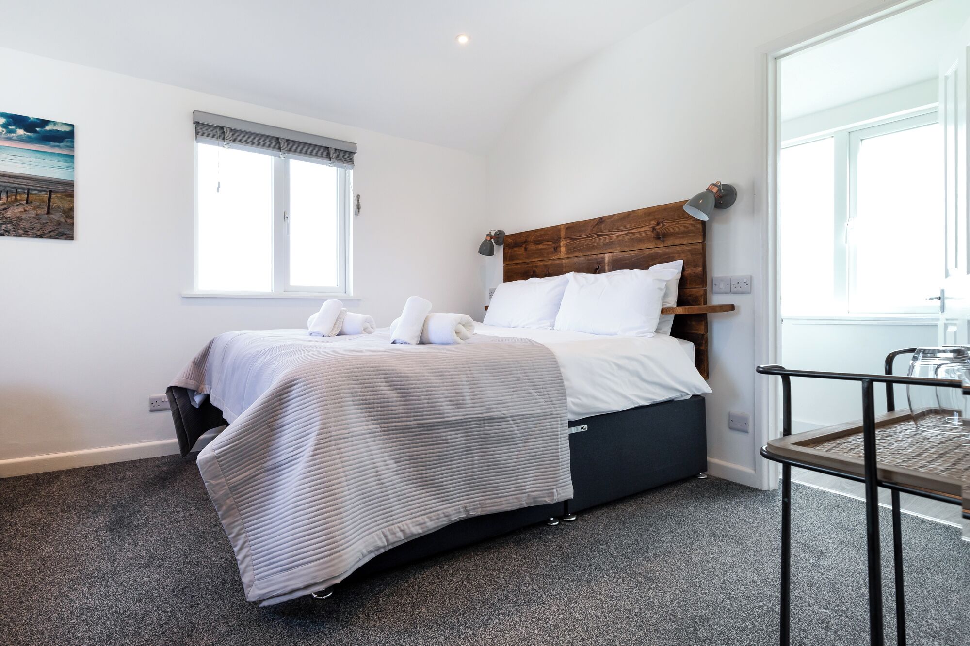 Una camera da letto con testiera in legno, un letto con lenzuola bianche, un tavolino e una finestra con persiane.