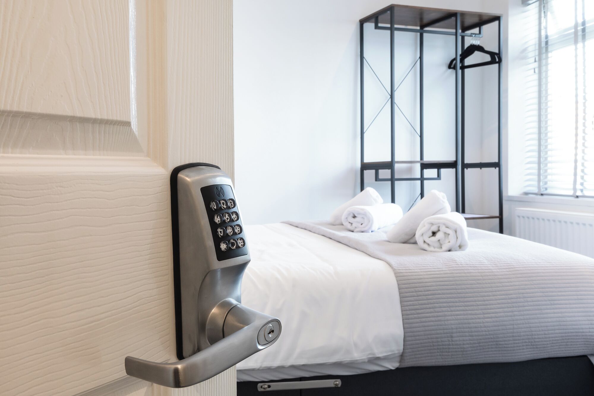 A hotel room with a modern door lock, a neatly made bed with white linens, and a window with blinds.