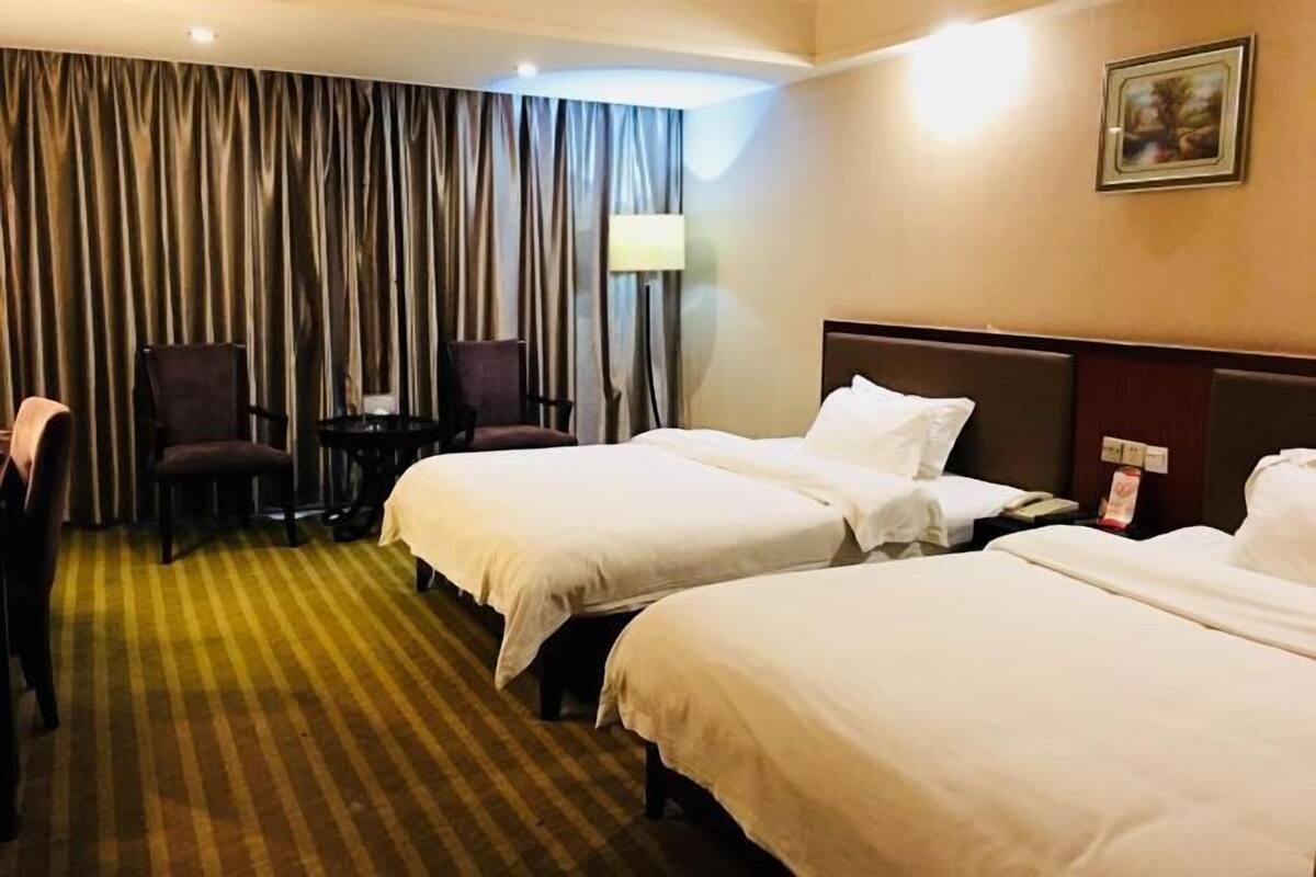 Une chambre d’hôtel avec deux lits, un bureau, une chaise, une lampe et un tableau au mur.