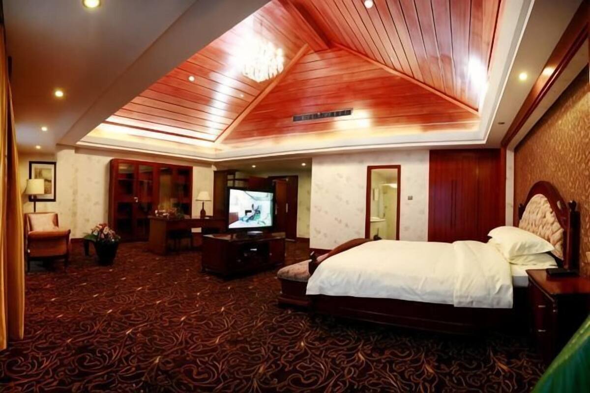 Une chambre d’hôtel avec un grand lit, une télévision, un bureau avec une chaise et un sol recouvert de moquette.