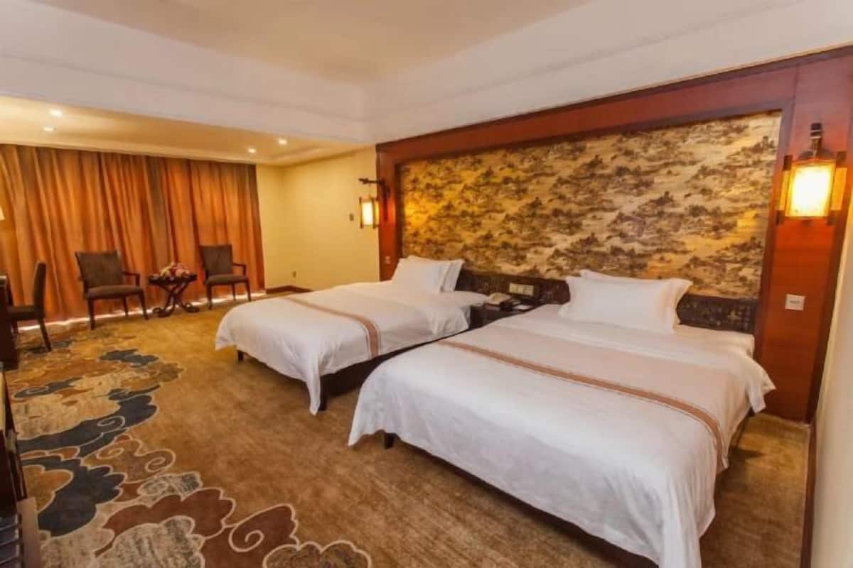 Une chambre d’hôtel avec deux lits, un sol recouvert de moquette, une tête de lit ornée d’un motif floral et une petite table avec des chaises.