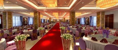 A banquet hall with a central red carpet aisle, round tables, and chairs.