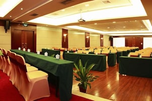 Un salón de conferencias con filas de mesas, sillas y una pantalla para proyector.