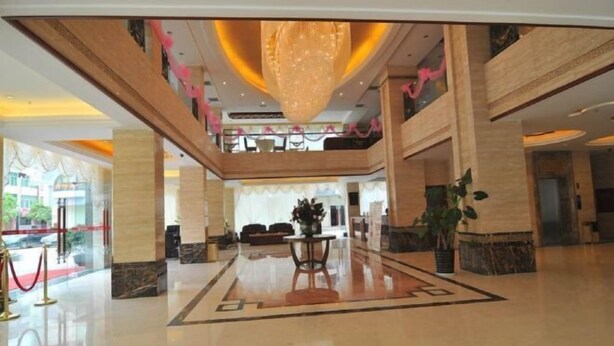 Een ruime lobby met een centraal hanglamp, een rood tapijt en een zithoek.