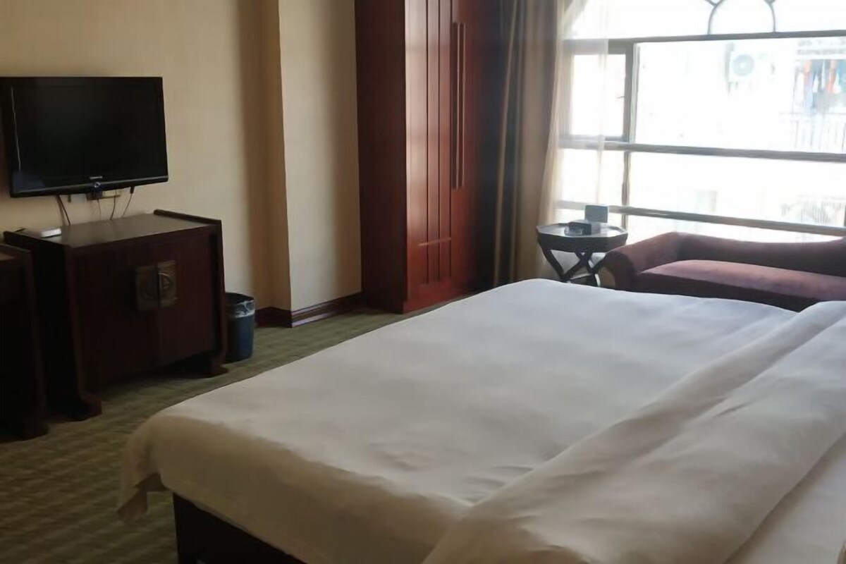 Habitación de hotel con una cama grande, televisión, una mesita y ventana con vistas al exterior.