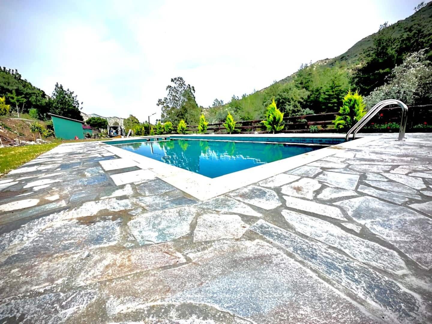 Una piscina amb terrassa de pedra, envoltada de vegetació i turons.